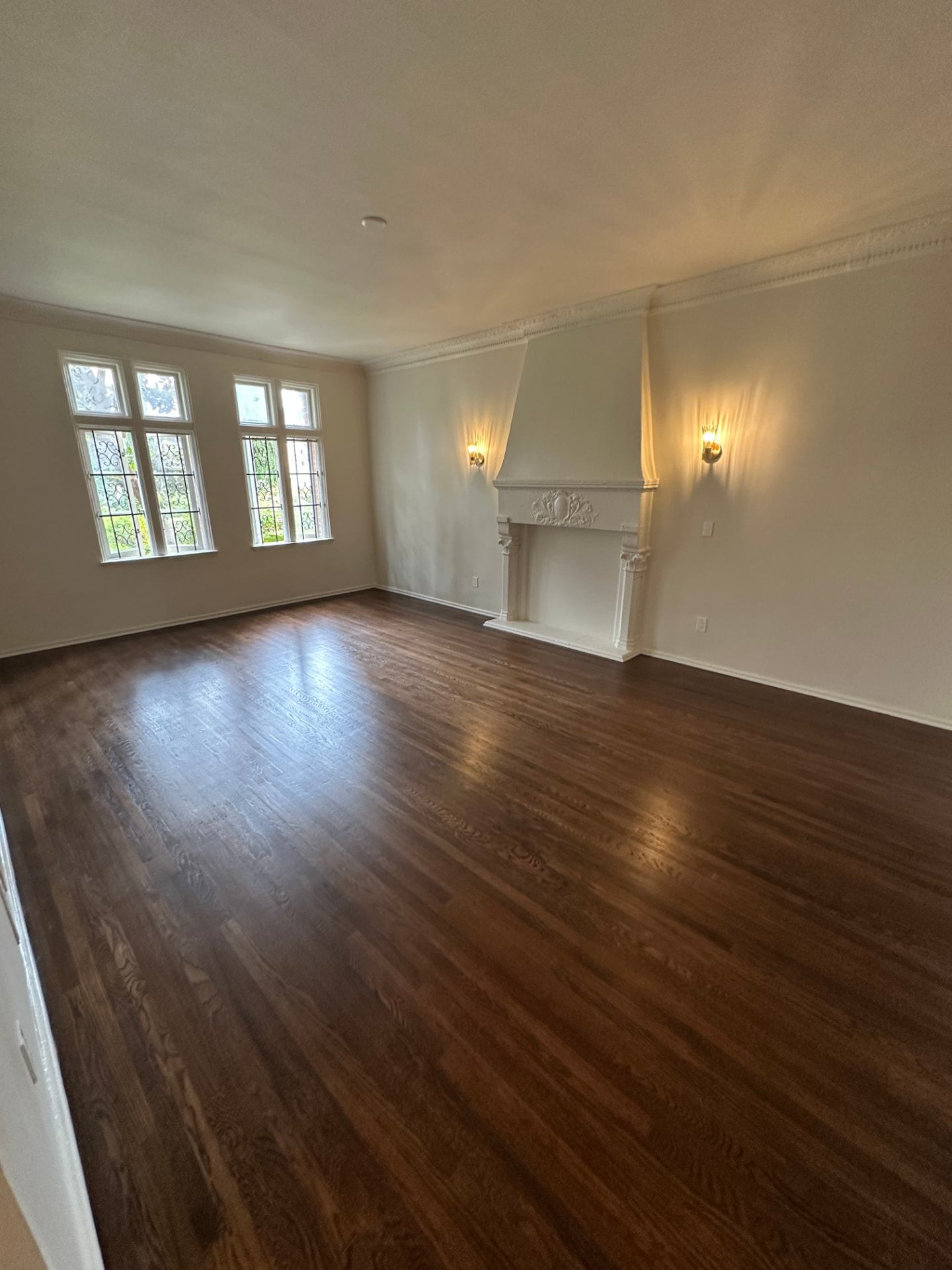 Living room in West Hollywood after an interior remodel, with refinished dark oak floors, restored crown molding, and cast mantel