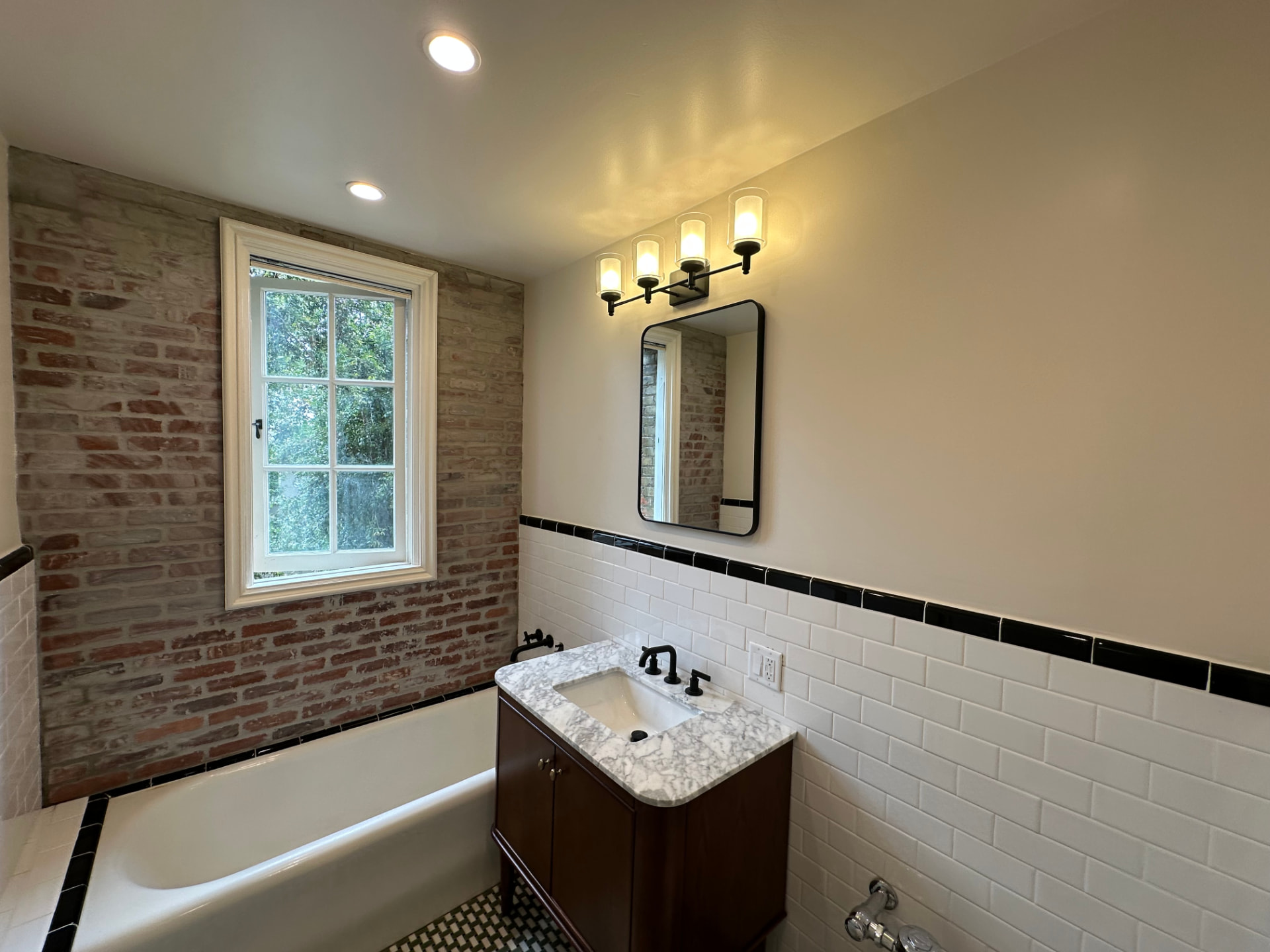 Bathroom renovation in Pacific Palisades with exposed brick wall, white subway tile, marble top vanity, and soaking tub