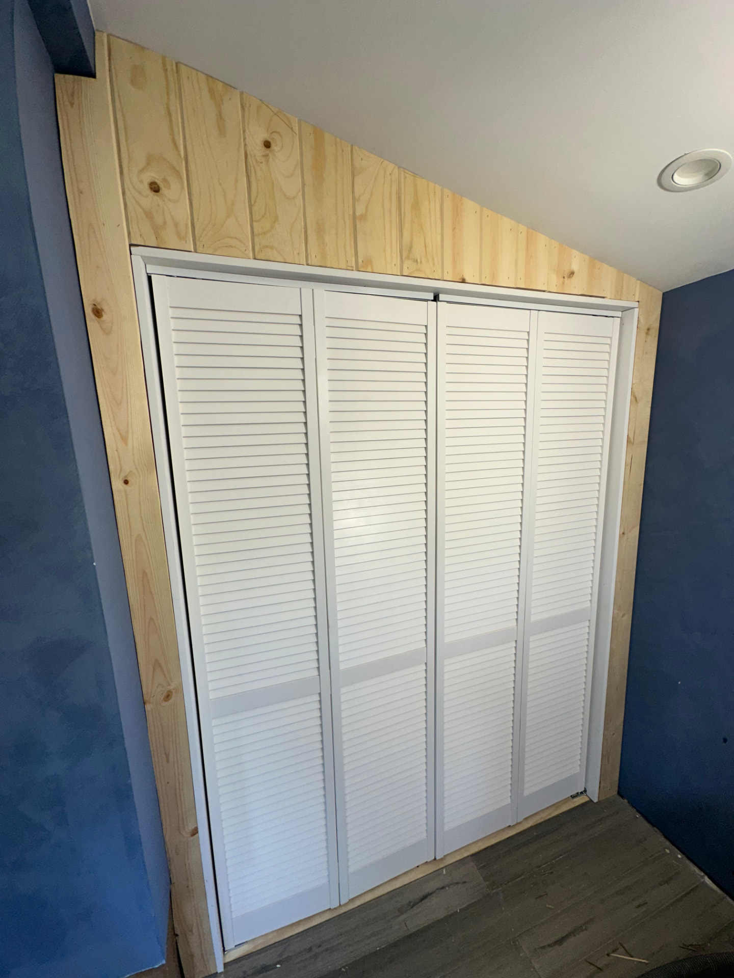 Finished built-in closet in Encino under a sloped ceiling with white louvered bifold doors, pine trim, and blue plaster walls