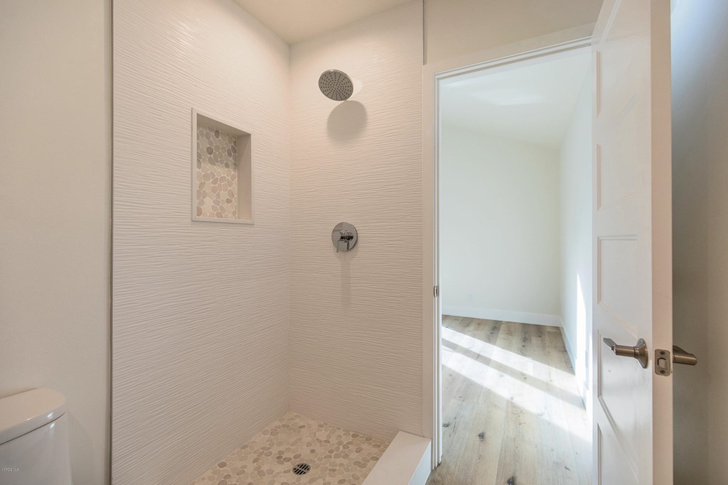 Walk-in shower in Brentwood with textured white wall tile, pebble tile floor and niche, rain shower head, and low bench
